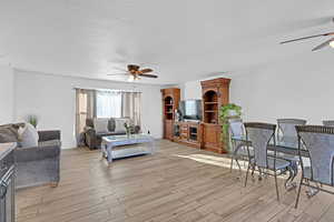 Living room featuring a textured ceiling, ceiling fan, and light wood-type flooring