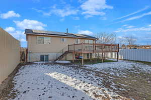 Snow covered back of property featuring a wooden deck and solar panels