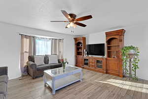 Living room featuring ceiling fan, a textured ceiling, and light wood-type flooring