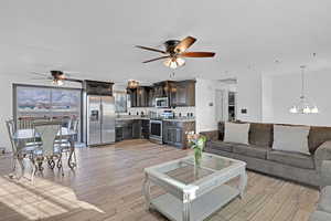 Living room featuring ceiling fan with notable chandelier, a textured ceiling, and light wood-type flooring