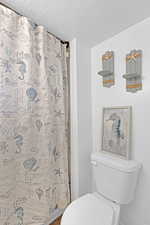 Bathroom featuring a shower with curtain, a textured ceiling, and toilet