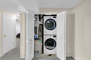 Clothes washing area featuring stacked washing maching and dryer and light carpet