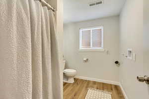 Bathroom featuring hardwood / wood-style flooring and toilet, laundry hookups.