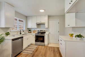 Kitchen with light wood-type flooring, appliances with stainless steel finishes, sink, and white cabinets