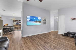 Living room with wood-type flooring, vaulted ceiling, and ceiling fan with notable chandelier