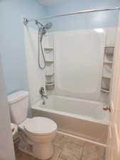 Bathroom featuring washtub / shower combination, tile patterned floors, and toilet