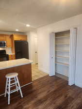 Kitchen featuring a textured ceiling, dark hardwood / wood-style flooring, a kitchen breakfast bar, kitchen peninsula, and black appliances