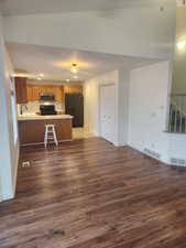 Kitchen featuring sink, stove, black fridge with ice dispenser, kitchen peninsula, and dark wood-type flooring