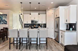 Kitchen featuring a breakfast bar, white cabinets, hanging light fixtures, stainless steel appliances, and a center island with sink