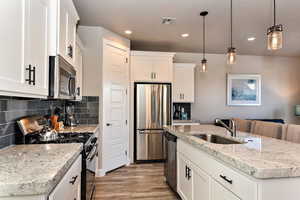 Kitchen with sink, white cabinetry, hanging light fixtures, appliances with stainless steel finishes, and a kitchen island with sink