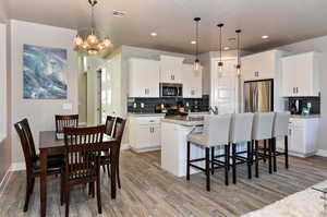 Kitchen featuring appliances with stainless steel finishes, white cabinets, and decorative light fixtures