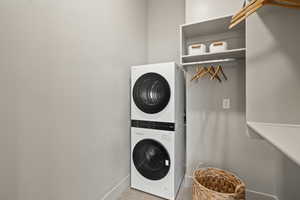 Clothes washing area featuring light tile patterned floors and stacked washing maching and dryer