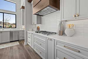 Kitchen with premium range hood, light stone counters, appliances with stainless steel finishes, dark hardwood / wood-style floors, and backsplash