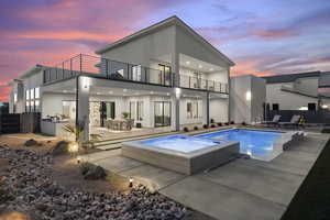 Back house at dusk with a swimming pool with hot tub, a patio area, and a balcony