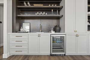 Bar with white cabinets, dark wood-type flooring, sink, and beverage cooler