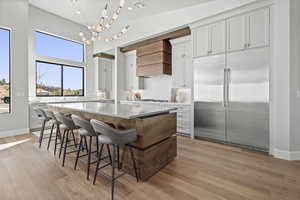 Kitchen with a breakfast bar, stainless steel appliances, a center island, light hardwood / wood-style floors, and custom range hood