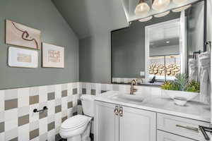 Bathroom with vanity, toilet, vaulted ceiling, and tile walls