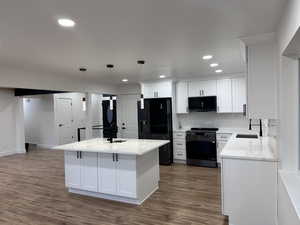 Kitchen featuring sink, black appliances, pendant lighting, light stone countertops, and white cabinets