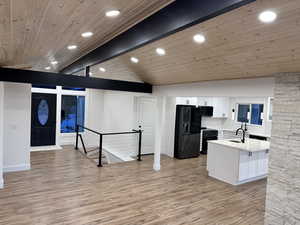 Kitchen featuring lofted ceiling with beams, white cabinets, a center island, black appliances, and light wood-type flooring