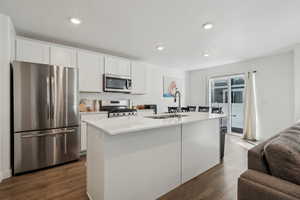 Kitchen with an island with sink, sink, white cabinets, dark hardwood / wood-style flooring, and stainless steel appliances