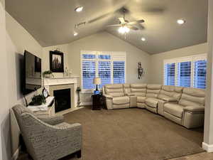 Living room featuring carpet floors, visible vents, a ceiling fan, vaulted ceiling, and a tile fireplace