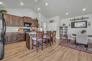 Kitchen featuring light hardwood / wood-style flooring, a kitchen island with sink, high vaulted ceiling, black appliances, and a kitchen bar