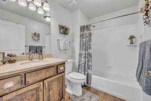 Full bathroom with hardwood / wood-style floors, a chandelier, vanity, shower / tub combo, and toilet