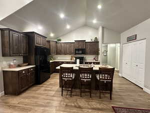 Kitchen with dark brown cabinetry, a sink, light countertops, black appliances, and an island with sink