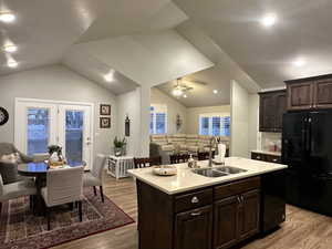 Kitchen featuring a sink, open floor plan, light countertops, black refrigerator with ice dispenser, and an island with sink