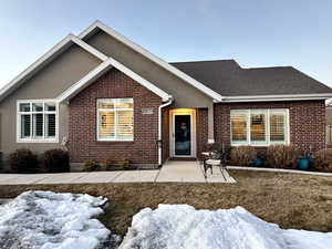 View of front of property featuring stucco siding, roof with shingles, a patio, and brick siding