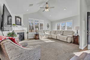 Living room featuring a tile fireplace, vaulted ceiling, light carpet, and ceiling fan