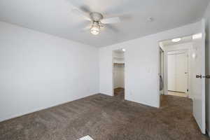 Unfurnished bedroom with dark colored carpet, a walk in closet, ceiling fan, and a closet