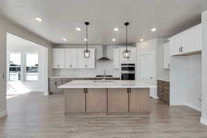 Kitchen with wall chimney range hood, white cabinets, and a center island with sink