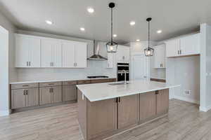 Kitchen featuring wall chimney exhaust hood, sink, black gas stovetop, a kitchen island with sink, and white cabinets