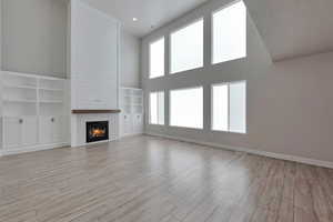 Unfurnished living room with a fireplace, a towering ceiling, light hardwood / wood-style flooring, and a healthy amount of sunlight