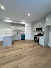 Kitchen with appliances with stainless steel finishes, sink, decorative backsplash, and light hardwood / wood-style flooring