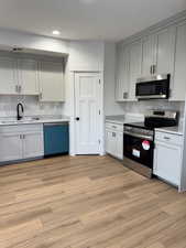 Kitchen with appliances with stainless steel finishes, sink, light hardwood / wood-style flooring, and backsplash