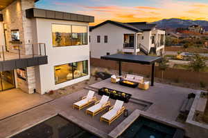 Back of house at dusk with stucco siding, a mountain view, a patio, and an outdoor living space with a fire pit