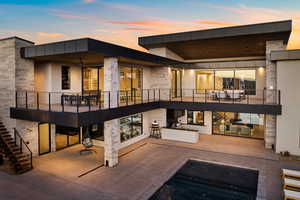 Back of property featuring ceiling fan, stone siding, a patio, and a balcony