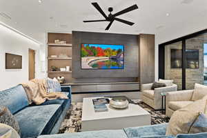 Living room with ceiling fan, an accent wall, and built in features