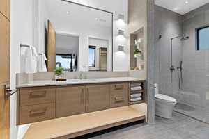 Full bathroom with toilet, tile patterned floors, tiled shower, and vanity