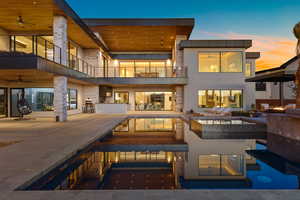 Back of house at dusk featuring an outdoor pool, ceiling fan, a balcony, and area for grilling