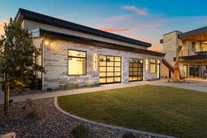 Back of house at dusk featuring stone siding and a lawn