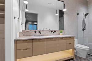 Full bath with toilet, a sink, tile walls, a tile shower, and double vanity