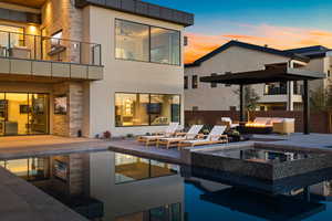 Back of house at dusk with a patio area, stone siding, stucco siding, and an in ground hot tub