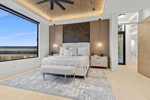 Bedroom with light wood finished floors, baseboards, visible vents, a raised ceiling, and a ceiling fan