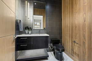 Bathroom featuring toilet, vanity, and tile walls