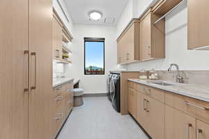 Clothes washing area featuring a sink, light floors, washing machine and dryer, and baseboards