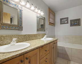 Bathroom with tile patterned flooring, tiled tub, and vanity