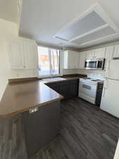 Kitchen with sink, white appliances, dark hardwood / wood-style floors, white cabinets, and kitchen peninsula